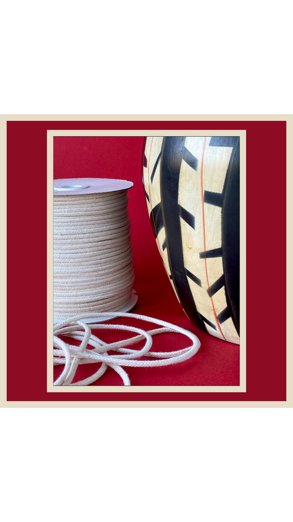 a reel of cotton rope sits next to a 1950's ceramic vase with a black and white tribal feather pattern. Both objects sit against a vivid red background